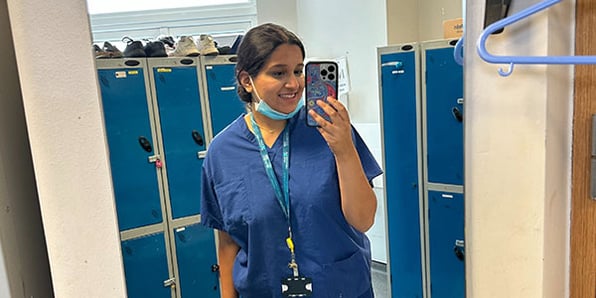 A person wearing blue scrubs taking a selfie in a mirror