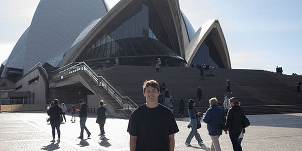 A person smiling and standing in front of the Sydney Opera House